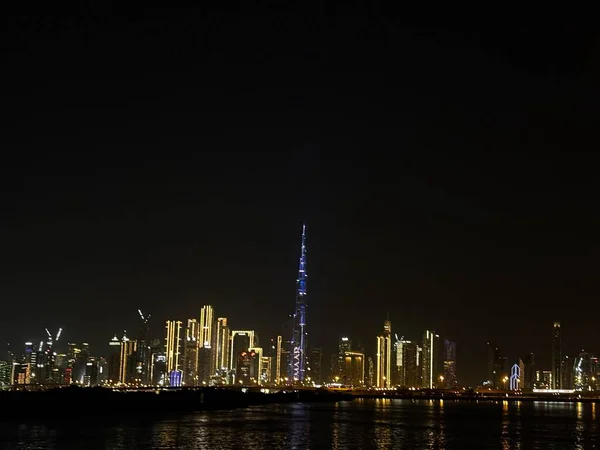 Dubai siluetinin gece görüşü ışıklarla aydınlandı. Burj Halife diğer binaların arasında dimdik ayakta duruyor. Sudaki yansıma..