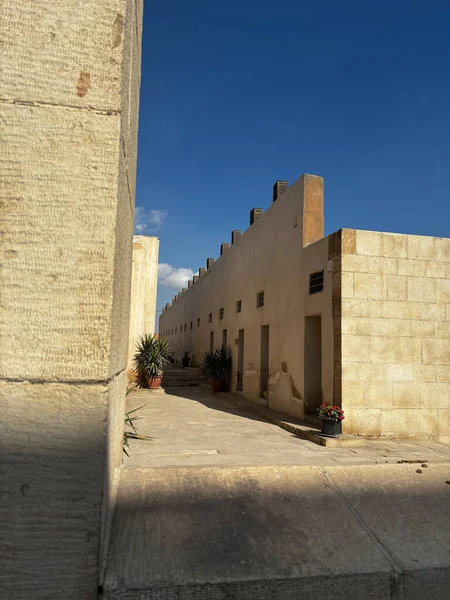 Kum taşı binaları açık mavi gökyüzünün altında dar bir yol çiziyor. Saksıdaki bitkiler çöl manzarasına biraz yeşillik katar..