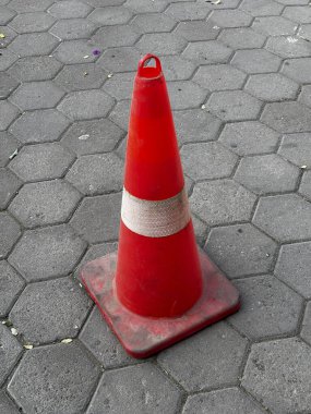 Gri altıgen döşeme yüzeyinde kırmızı ve beyaz trafik konisi.