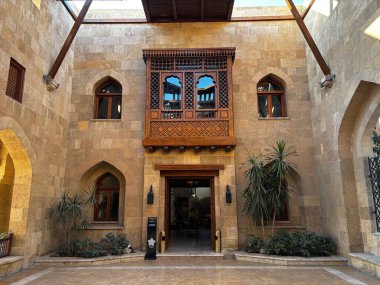 Ahşap balkon ve kemerli pencerelerle süslü bina cephesi. Kum taşı duvarlar ve dekoratif bitkiler.