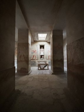 Sütunlarda ve duvarlarda resimler olan antik bir mezar ya da tapınağın iç görünüşü, bir heykele götürüyor..