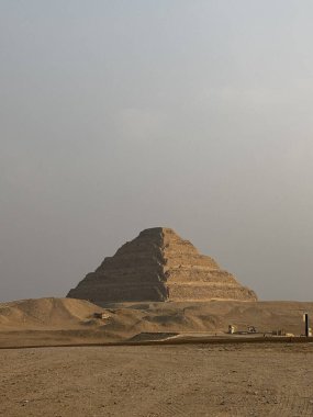 Djoser Piramidi, bir basamak piramit, puslu bir gökyüzünün altında çöl manzarasından yükselir..