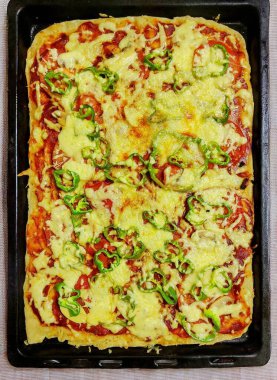 Siyah tepside dikdörtgen pizza. Pizzanın üstünde peynir, sos ve yeşil biber var..