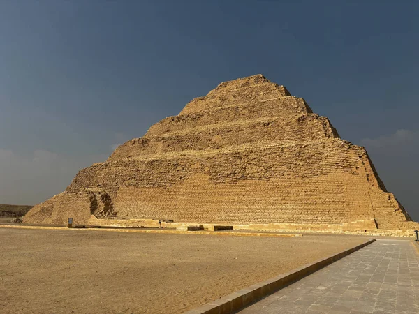 Mısır 'ın Saqqara kentindeki Djoser piramidi, açık mavi bir gökyüzünün altında. Kumlu bir çöl manzarasında antik mimari.
