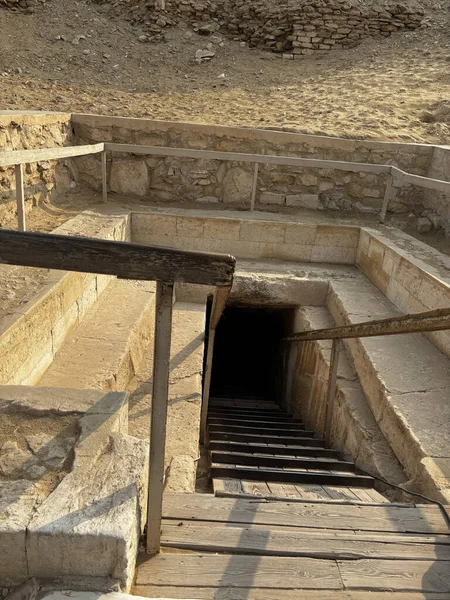 Karanlığa doğru inen tahta merdivenleri olan bir yeraltı mezarına ya da yapısına giriş. Taş yapısı görünür.