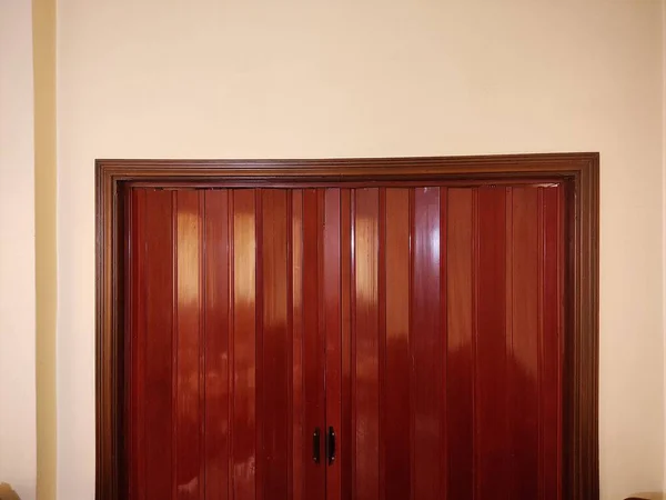 Koyu süslemeli kırmızı bir akordeon tarzı kapı beyaz bir duvara monte edilir. Kapıda iki siyah düğme var..