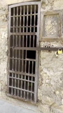 Başlangıçta hafifçe aralık bırakılan metal parmaklıklı bir kapı sırayla kapatılıyor. Karanlık bir iç mekan ortaya çıkarıyor..