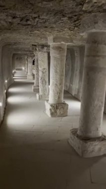 Uzunluğu boyunca uzanan kare taş kolonlara sahip bir tünel. Loş ışıklandırma koridoru aydınlatıyor, desenli taş duvarları ve tavanı aydınlatıyor.