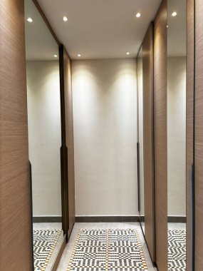 Dar koridor, aynalı gardıroplar, desenli ahşap döşemeler ve desenli halı. Dahili ışıklandırmalı modern tasarım.