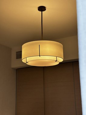 Aydınlatılmış davul kolyesi. Tavandan sarkan, kapısı olan ve beyaz olmayan bir odada..