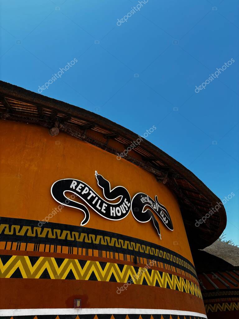 Building featuring Reptile House signage with snake illustration. Blue sky backdrop, ethnic tribal graphic on facade.