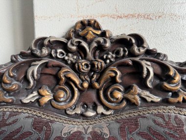 Süslü, antika bir sandalyenin yakın çekimi. Altın, gümüş ve kahverengi desenli döşemeleri olan karmaşık oymalar..