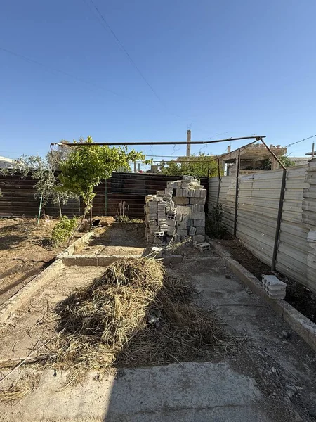 Açık havada gri tuğlalar, bazı metal yapılar ve açık mavi bir gökyüzünün altında kuru çimenler yer alıyor..