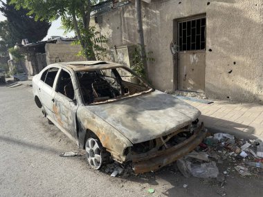 Bir binanın yanındaki caddede parçalanmış bir araba. Araba yanmış ve ağır hasar görmüş..