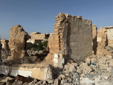 Bir binanın yıkıntıları, muhtemelen çatışmadan ya da doğal afetten. Enkaz ve hasarlı duvarlar berrak ve parlak bir gökyüzünün altında görülebilir..