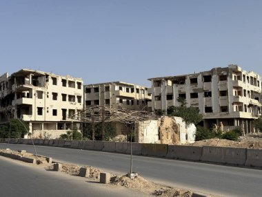 Savaşın yıktığı binalar açık bir gökyüzüne karşı duruyor. Yapılar büyük ihtimalle çatışmadan dolayı ağır hasar görmüş..