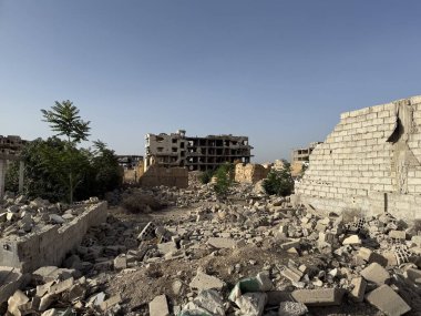 Açık mavi gökyüzünün altında savaştan zarar görmüş binalar ve molozlar. Bu şehir manzarasında yıkım ve yıkım açıkça görülüyor..