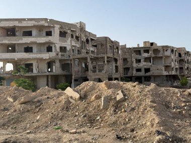 Yıkılmış binalar molozların arasında duruyor, muhtemelen savaş sonrası ya da büyük bir felaket. Binalar ağır hasar görmüş ve çıplak..