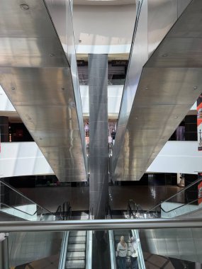 Çok katlı bir binadaki yürüyen merdivenlere bakıyorum. Gümüş metal ışığı yansıtır. Bazı insanlar yürüyen merdivenlerden görülebiliyor..