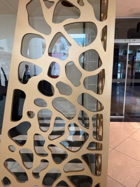 Bulanık şekilli yansıtıcı yüzeylerin önündeki modern altın desenli bölücü / duvar. İç tasarım ögesi.