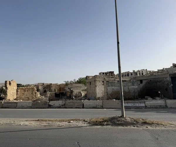 Savaşın yıktığı binalar ve yıkıntılar bir yol çizgisi. Yol kenarında bir elektrik direği duruyor. Yukarıdaki mavi gökyüzü. Büyük olasılıkla Orta Doğu ayarı.