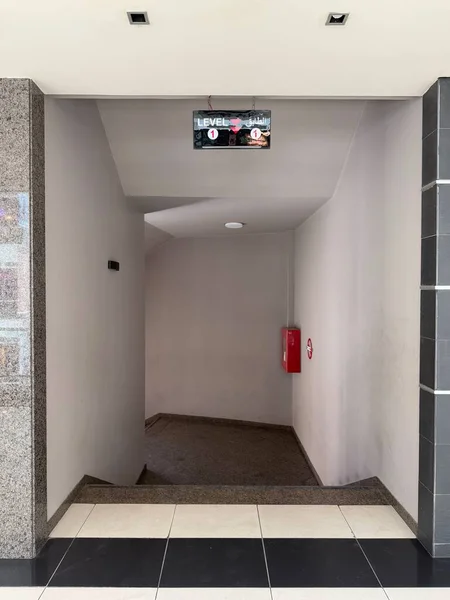 Merdiven boşluğuna bakarken çekilmiş. Duvarlar beyaz ve fayanslar görülebilir. Sol tarafta duvardaki tabela görülüyor..