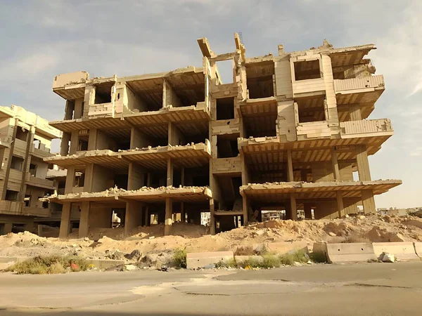 Savaşın yıktığı bina. Harap olmuş yapı, enkaz ve çöl ile çevrili bulutlu bir gökyüzüne karşı beton bir iskelet..