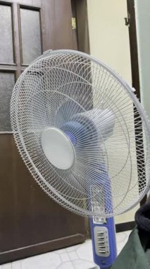 * * Mavi ve beyaz bir vantilatör aktif olarak dönüyor, hafif bir esinti yaratıyor. Bıçaklar hareket yüzünden bulanık. İyi misin?