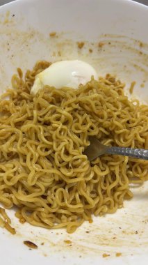 Bir kase rafadan yumurtalı erişte, çatalla yeniyor. Yakın çekim, kasenin bir kısmının lekeli olduğunu gösterir..