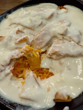 Gevrek elementlerle dolu kremalı bir tabağın yakın çekimi. Yiyecek katmanlı ve beyaz sosla kaplanmış gibi görünüyor..