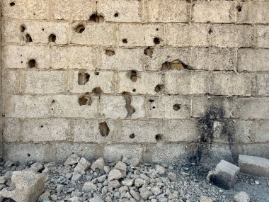 Çatışma veya yıkım anlamına gelen tabanında sayısız kurşun deliği ve kırık enkaz bulunan hasarlı beton blok duvarı.