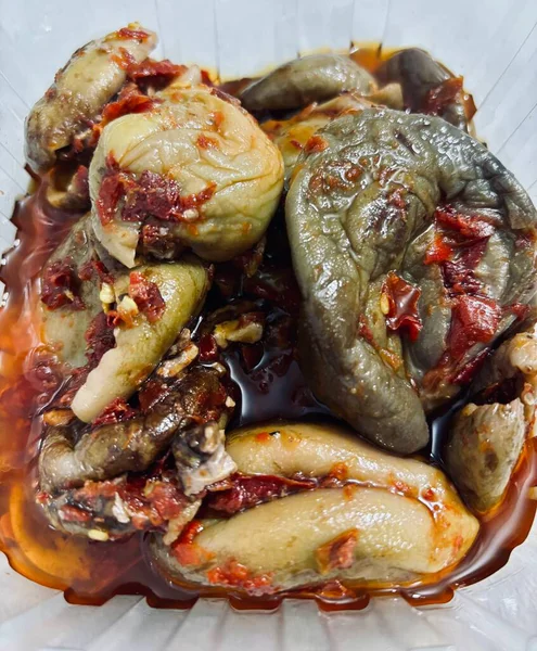 Plastik bir kabın içinde içi doldurulmuş patlıcan, görünür domates ve baharat parçacıkları ile sıvıya batırılmış..