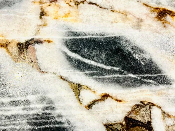 Beyaz, gri, siyah ve altın damarlı cilalı mermer bir levhanın yakın çekimi. Soyut doğal taş dokusu.