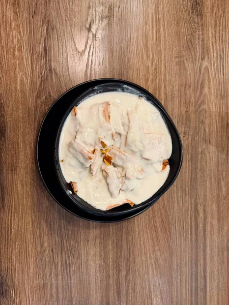 Kremalı beyaz sosla kaplanmış, ahşap bir masaya yerleştirilmiş, siyah bir kâsenin yukarıdan görünüşü..