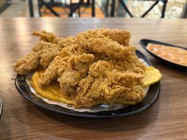 Tahta bir masanın üzerinde, yanında sos olan, çıtır çıtır tavuk filetosu yığını..