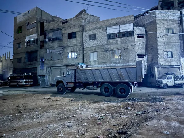 Şam, Suriye - 10: 20 2025: kaba, kentsel bir çevrede park etmiş bir çöp kamyonunu gösteren gece sahnesi. Arka plandaki binalar. Sokak manzarası, inşaat alanı.