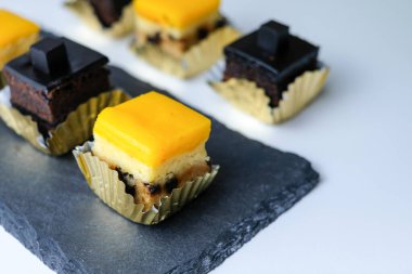 Beyaz arka planda siyah tahtada servis edilen çikolatalı ve sarı mangolu mini turtalı kekler. Fırın, tatlı menüleri, yemek tasarımı, minimalist tatlı için mükemmel.