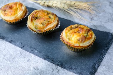 Üç adet altın hamurlu ve kremalı ev yapımı tart, temiz desenli arka planı olan siyah bir tahtaya güzelce yerleştirilmiş. Fırın promosyonları ve tatlı menüleri için mükemmel.