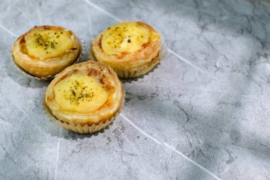 Temiz desenli arka plana yerleştirilmiş üç adet altın kabuklu ve kremalı ev yapımı mini tart. Fırın promosyonları ve tatlı menüleri için mükemmel.
