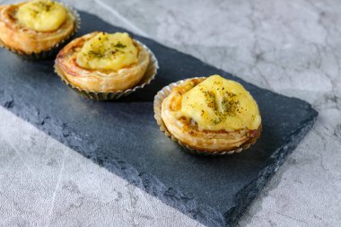 Üç adet altın hamurlu ve kremalı ev yapımı tart, temiz desenli arka planı olan siyah bir tahtaya güzelce yerleştirilmiş. Fırın promosyonları ve tatlı menüleri için mükemmel.