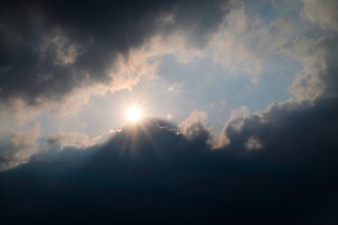 Güneş ışığı dramatik bir gökyüzünde kara bulutların arasından kırılıyor, ışık ve gölge arasında güçlü bir kontrastlık yaratıyor. İlham verici, hava durumu, umut, inanç ve doğa güzelliği için mükemmel.