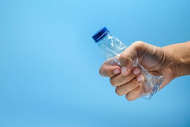 Mavi kapaklı temiz bir plastik şişeyi parlak mavi bir arka planda ezen bir adam. Geri dönüşüm, çevre bilinci, plastik atık azaltma ve çevre dostu alışkanlıklar için uygundur