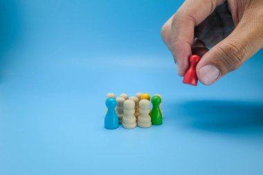 Bir el, çok renkli ve nötr tahta piyonlardan kırmızı tahta bir figür seçiyor. Liderliği, karar vermeyi ve işe alınmayı sembolize ediyor. Takım oluşturma, insan kaynakları ve liderlik için ideal.