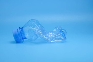 Temiz mavi arka planda koyu mavi kapaklı ezilmiş tek bir plastik şişe plastik atıkları, geri dönüşümü sembolize eder. Sürdürülebilirlik, atık yönetimi ve eğitime uygundur