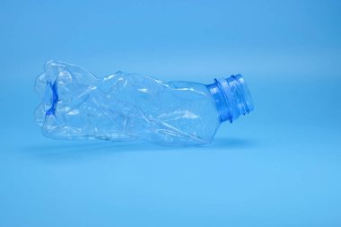 Temiz mavi arkaplana yerleştirilmiş tek bir ezilmiş plastik şişe plastik atıkları, geri dönüşümü simgeler. Sürdürülebilirlik, atık yönetimi ve eğitime uygundur