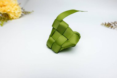Bayram kutlamalarıyla ilişkilendirilen temiz beyaz arkaplana ketupat adlı yeşil kurdele dekorasyonunun yakın çekimi. Ramazan 'da veya bayram tanıtım materyallerinde kullanım için mükemmel