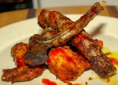 Lezzetli bir ızgara et, kuzu pirzolası ve tavuk parçaları, parlak, baharatlı kırmızı sosla kaplanmış, beyaz bir tabakta servis edilir..