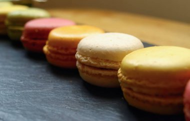 Koyu dokulu bir yüzeyde sanatsal bir şekilde düzenlenmiş çeşitli renklerde klasik Fransız badem kurabiyelerinden oluşan canlı bir seçim, tadını çıkarmaya hazır..