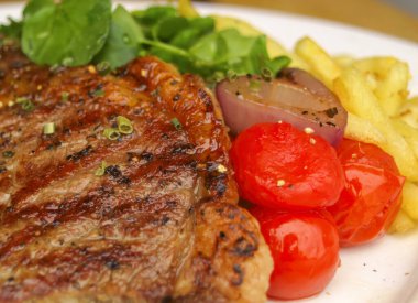 Lezzetli bir pirzola bifteği, yanında canlı vişneli domates, çıtır patates kızartması ve taze su teresi..