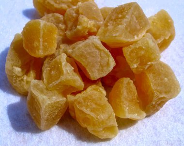 Tatlı, baharatlı ve çiğnenmiş dokularını parlak bir arka planda sergileyen, altın rengi kristalize edilmiş zencefil küpleri..